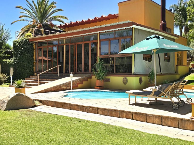 Outdoor pool area featuring a paved deck, swimming pool, and an enclosed patio with ramp access, set against a landscaped garden.