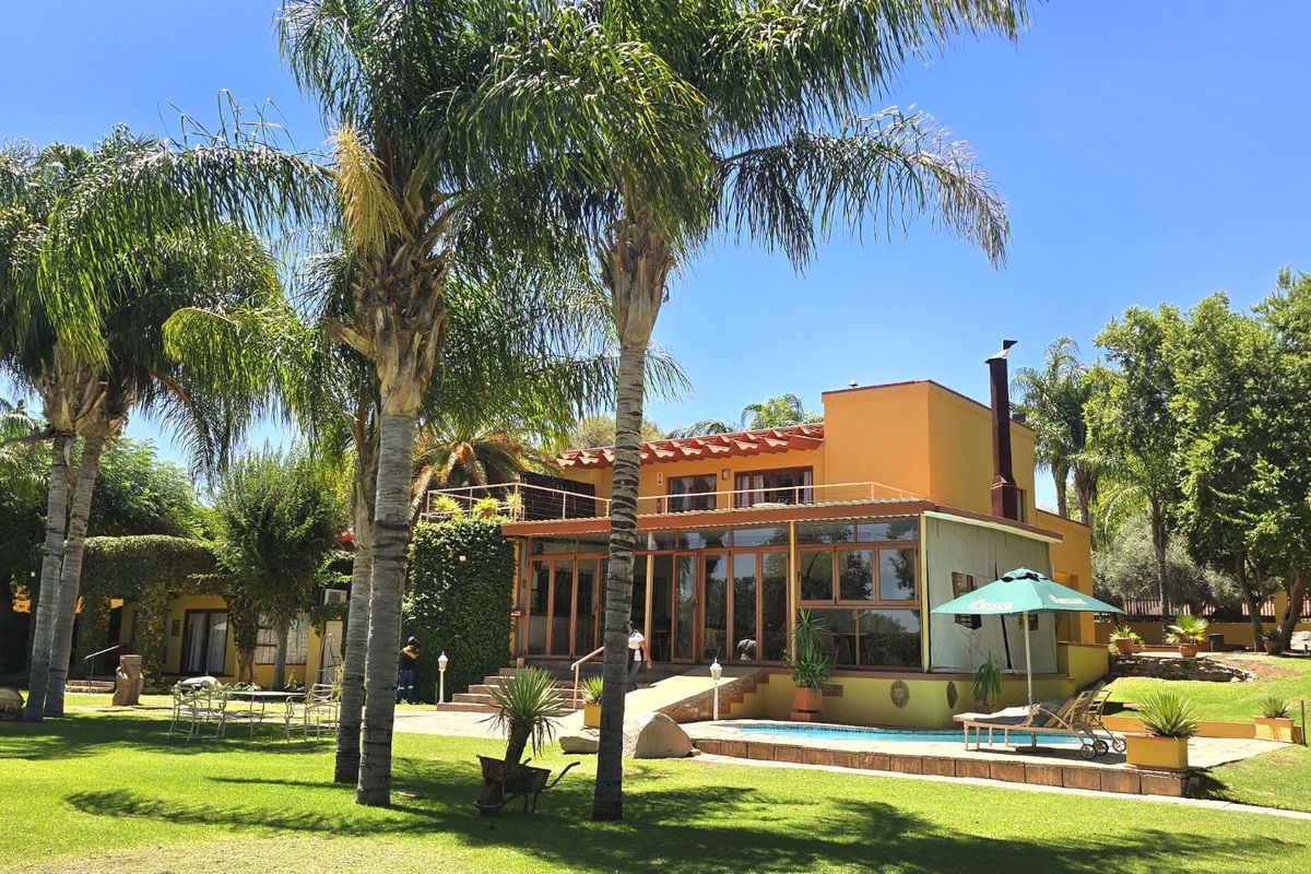 Rear view of the commercial property featuring a swimming pool, expansive lawn, landscaped gardens, and a terrace with balcony access.