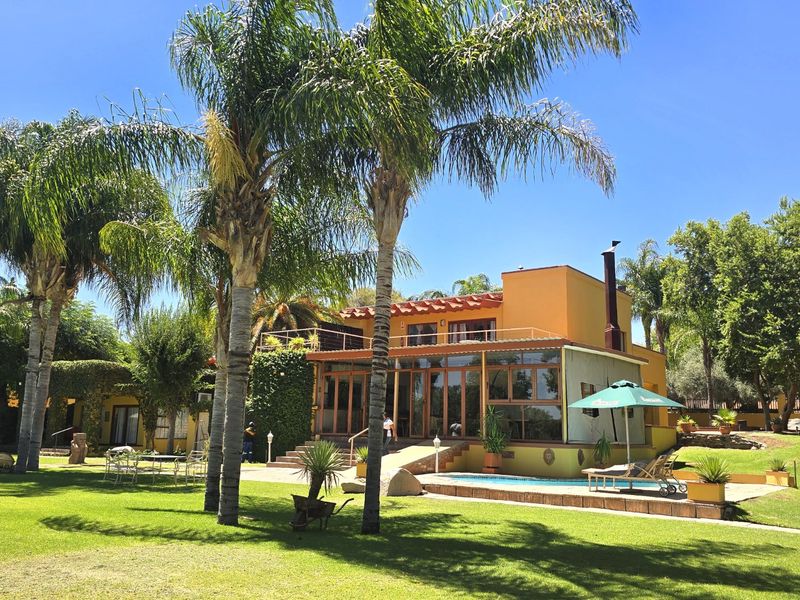 Rear view of the commercial property featuring a swimming pool, expansive lawn, landscaped gardens, and a terrace with balcony access.