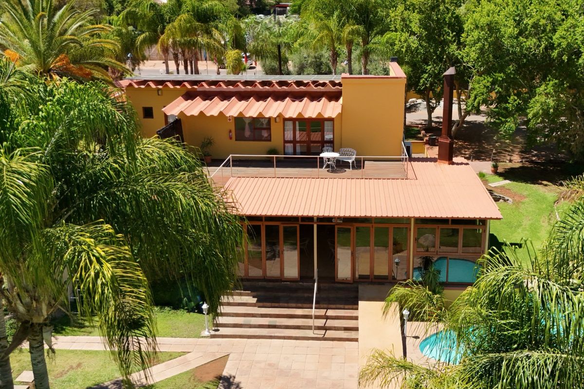 Aerial view of a commercial property featuring a swimming pool, landscaped garden, tiled patio, and a multi-level building with a metal roof and balcony.