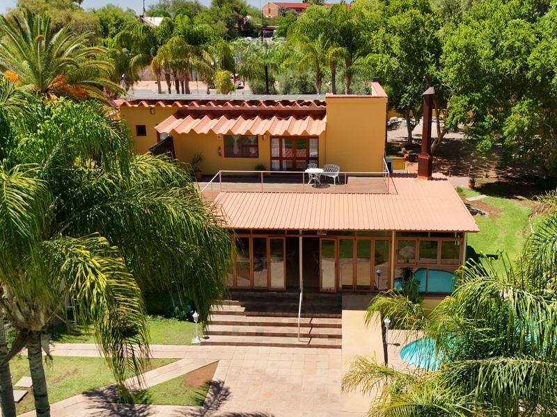 Aerial view of a commercial property featuring a swimming pool, landscaped garden, tiled patio, and a multi-level building with a metal roof and balcony.