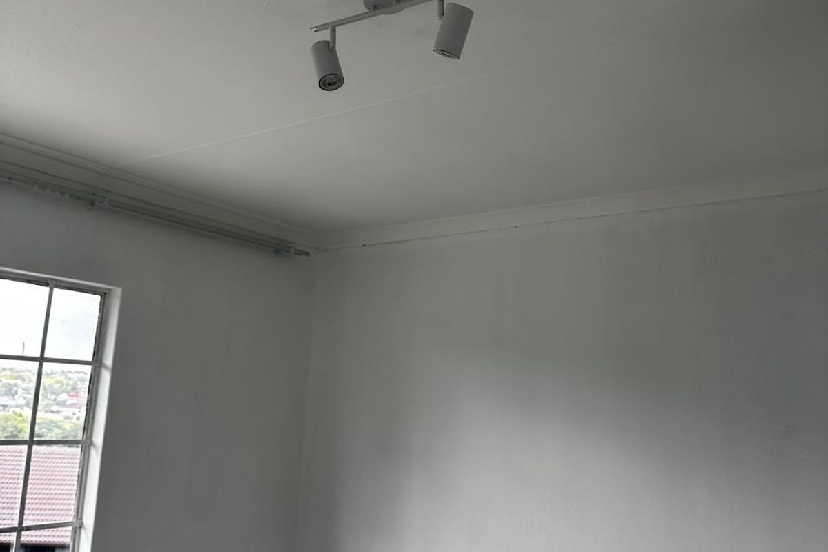 A simple, empty room featuring tiled flooring, a window with security bars, and a modern adjustable spotlight fixture on the ceiling.