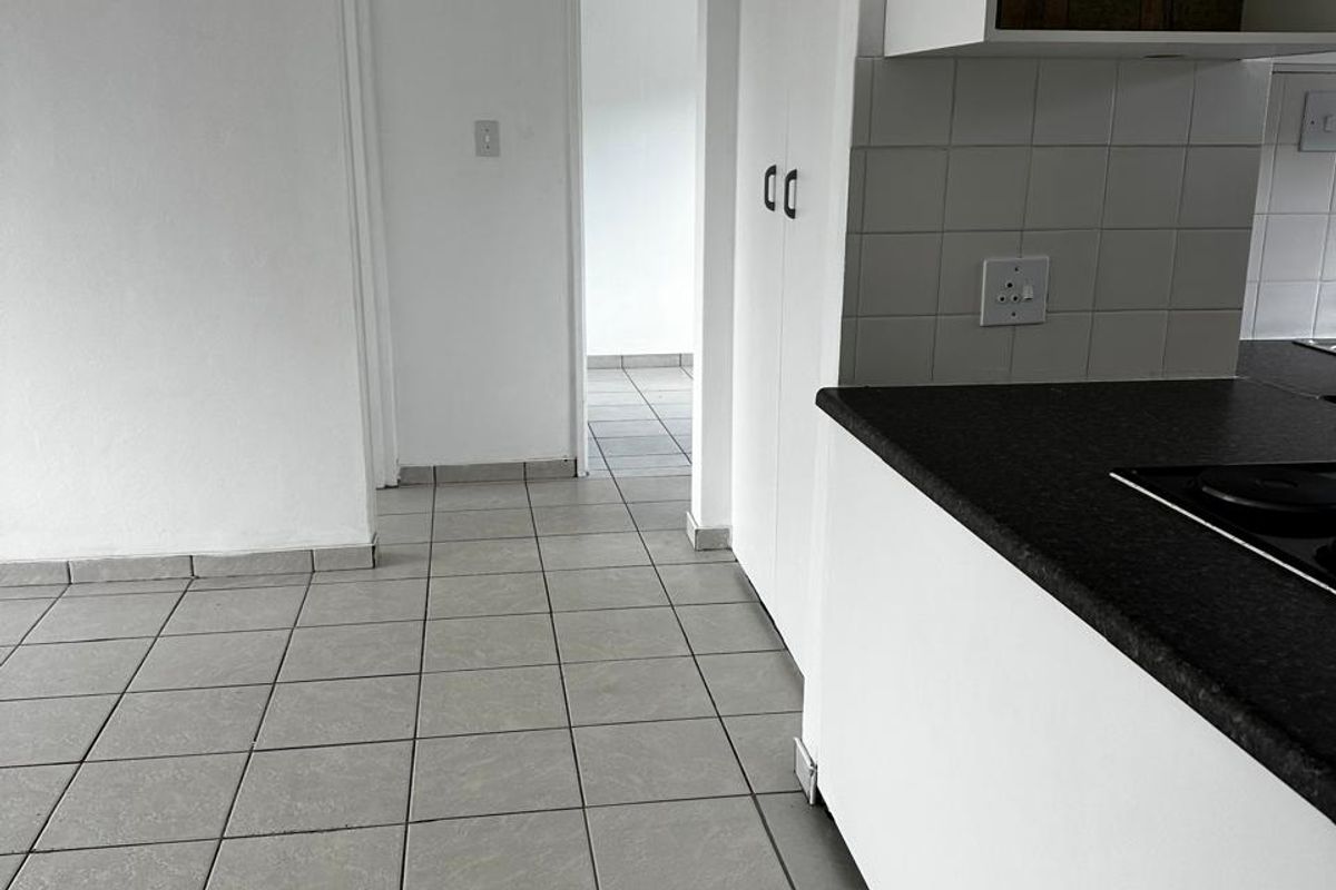 A view of a kitchen area featuring dark countertops, built-in cabinetry, and tiled flooring, leading into a hallway.