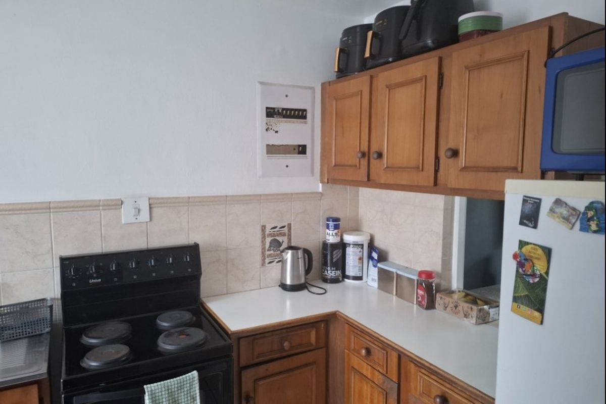 A functional kitchen featuring traditional wooden cabinetry, laminate countertops, and a ceramic tile backsplash with a freestanding electric stove.