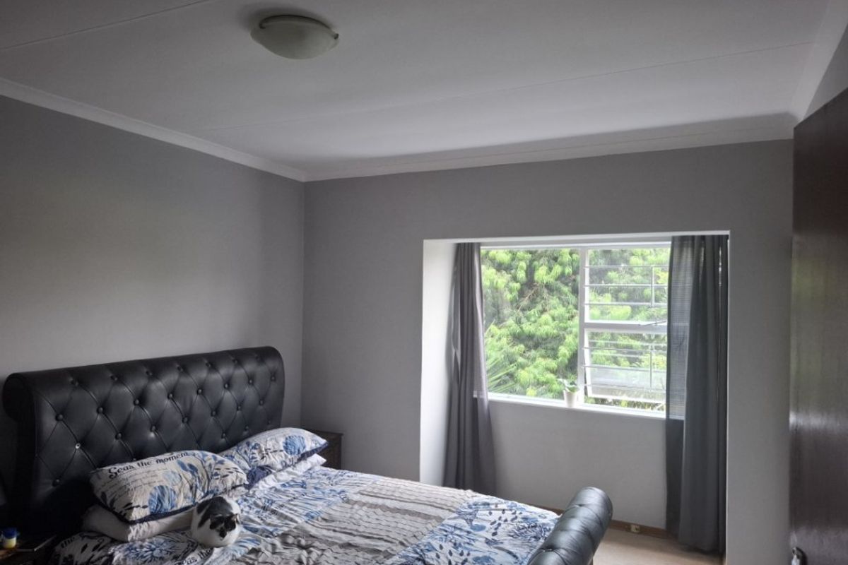 A bedroom featuring neutral grey walls, a coved ceiling, and a window fitted with security bars overlooking greenery.