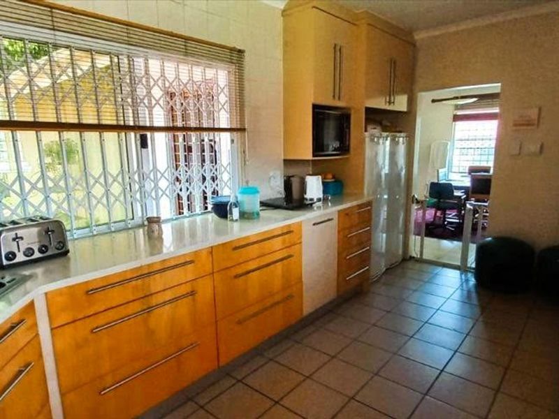 A functional kitchen featuring wood-tone cabinetry, stone countertops, and tiled flooring, with a window security gate and direct access to an adjacent room.