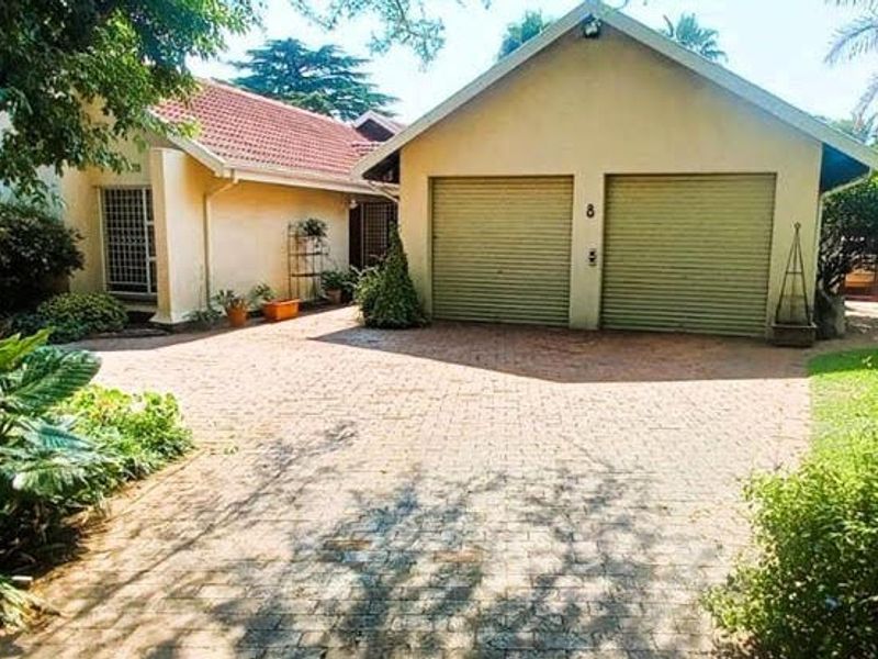 Front view of the property featuring a paved driveway leading to a double garage with roller shutter doors and a tiled roof.