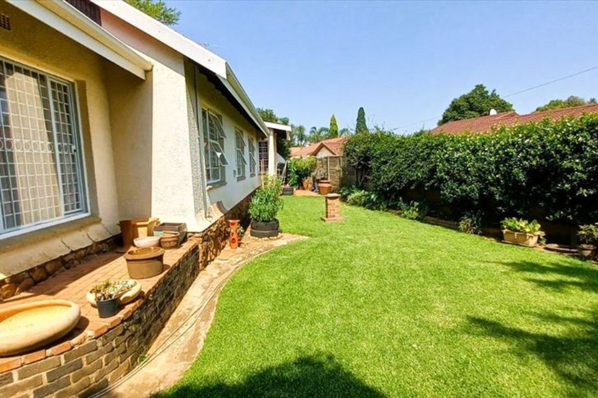 A well-maintained rear garden featuring a manicured lawn, established hedging, and a brick retaining wall along the side of the house.