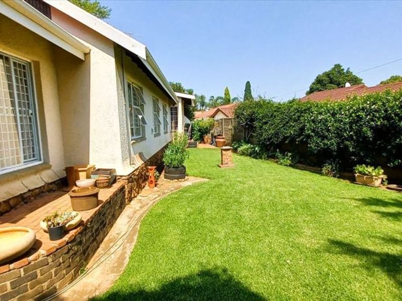 A well-maintained rear garden featuring a manicured lawn, established hedging, and a brick retaining wall along the side of the house.