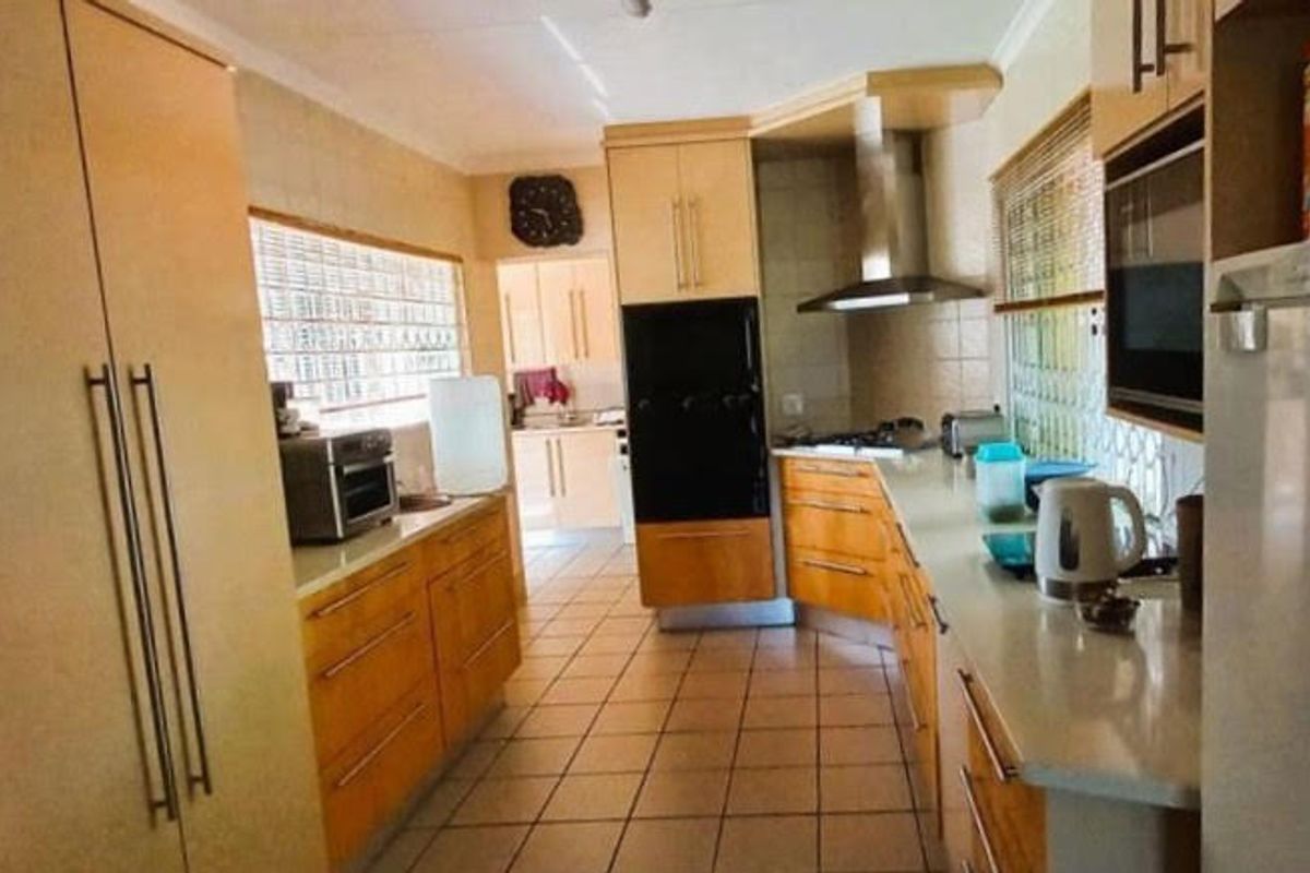A functional kitchen featuring wood-toned cabinetry, built-in oven, stainless steel extractor fan, and tiled flooring with natural light from glass block windows.