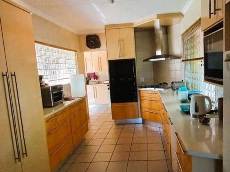 A functional kitchen featuring wood-toned cabinetry, built-in oven, stainless steel extractor fan, and tiled flooring with natural light from glass block windows.