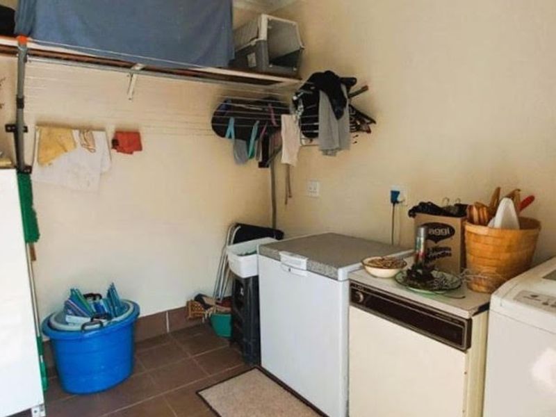 A functional laundry area featuring tiled flooring, wall-mounted storage shelving, and dedicated plumbing and electrical points for appliances.
