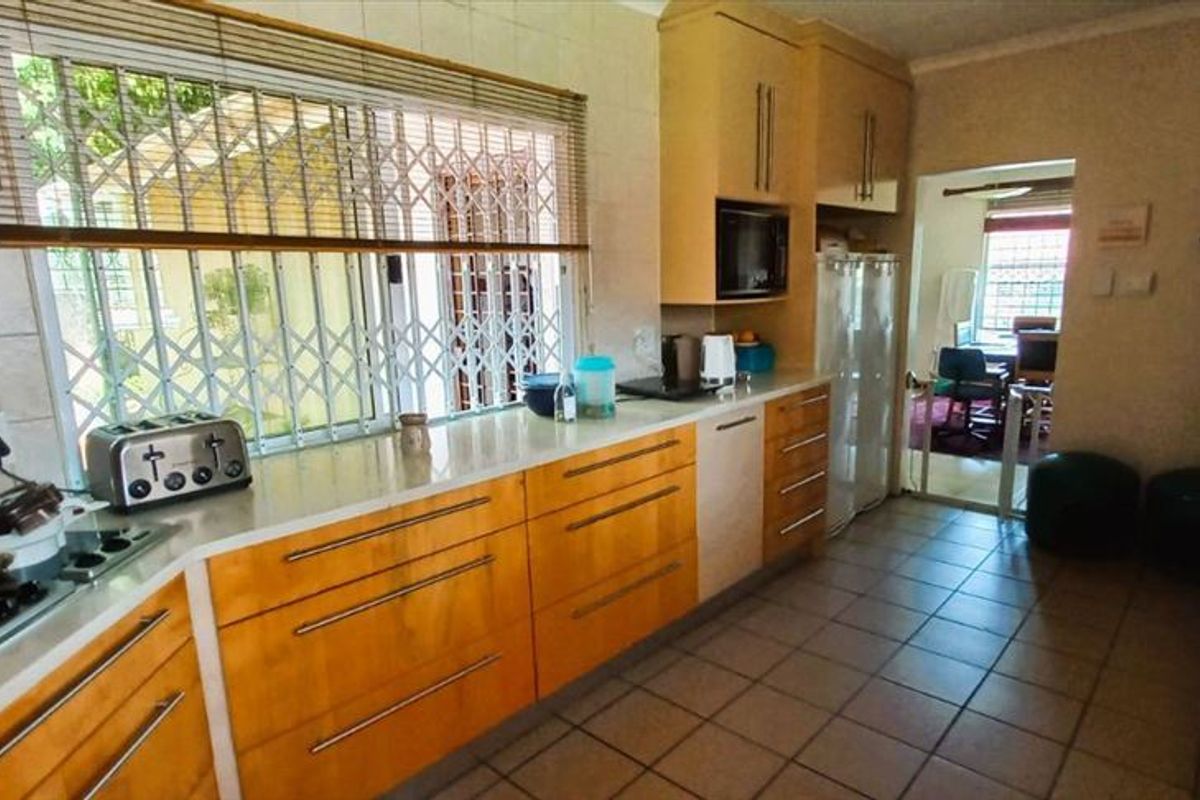 A functional kitchen featuring wooden cabinetry, a gas hob with extractor fan, built-in microwave, and tiled flooring, with a view into an adjacent room.