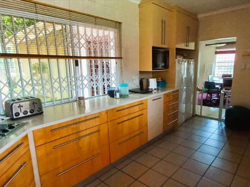 A functional kitchen featuring wooden cabinetry, a gas hob with extractor fan, built-in microwave, and tiled flooring, with a view into an adjacent room.