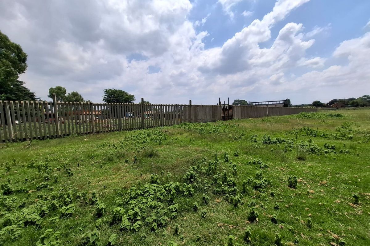 A view of a vacant residential plot featuring established grass and concrete palisade perimeter fencing.