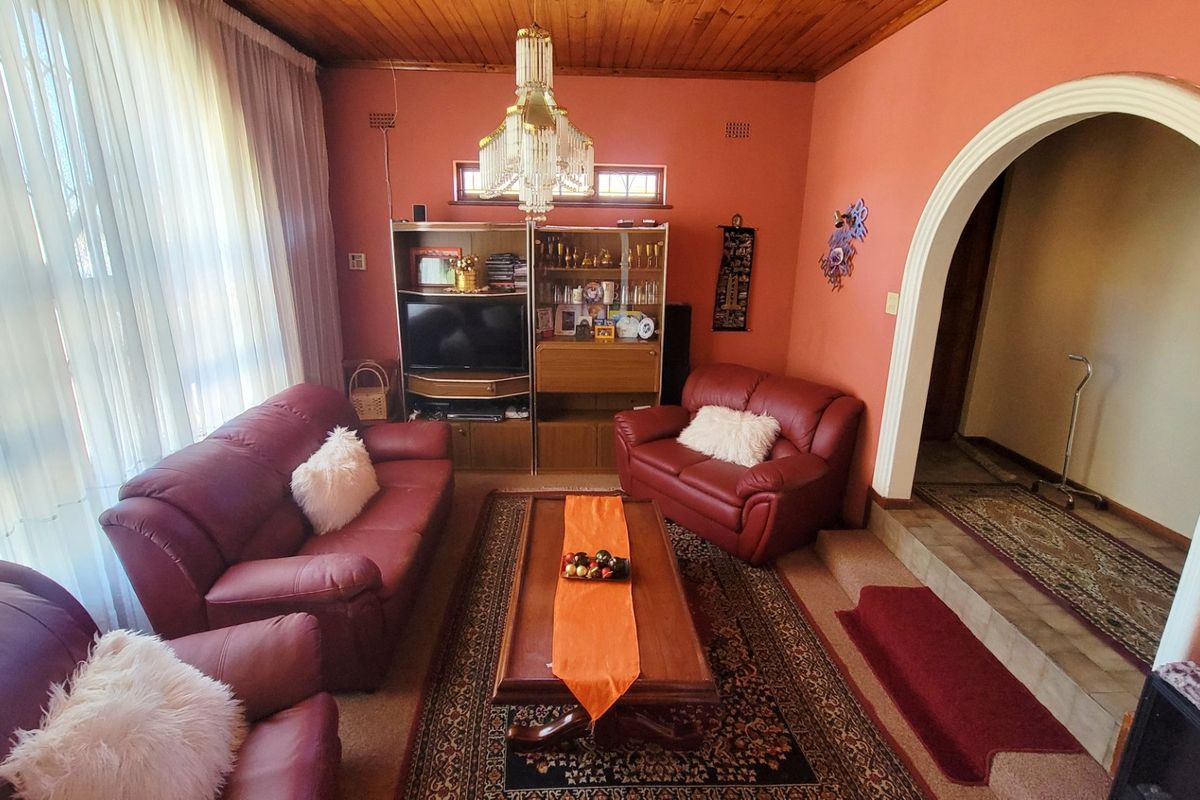 A traditional living room featuring a timber-paneled ceiling, an arched entryway, and large windows with sheer curtains.