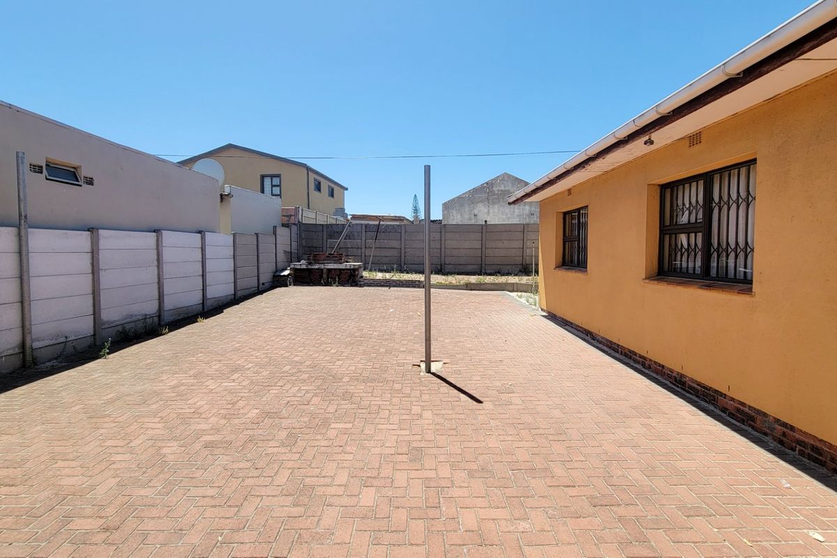 A paved rear courtyard area featuring perimeter boundary walls, security bars on windows, and a central washing line pole.