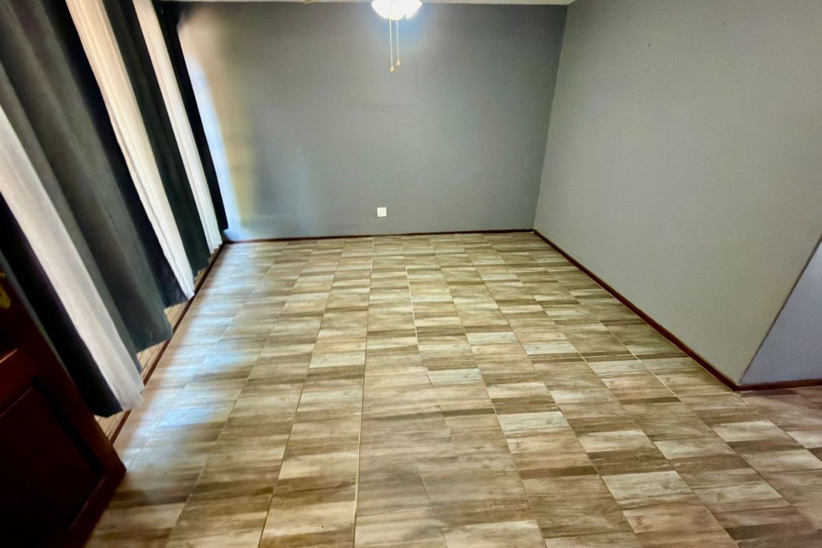 An empty living room featuring tiled flooring, a ceiling fan, and neutral grey walls, offering a blank canvas for interior design.