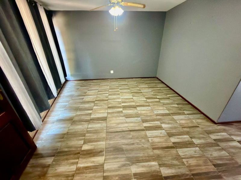 An empty living room featuring tiled flooring, a ceiling fan, and neutral grey walls, offering a blank canvas for interior design.