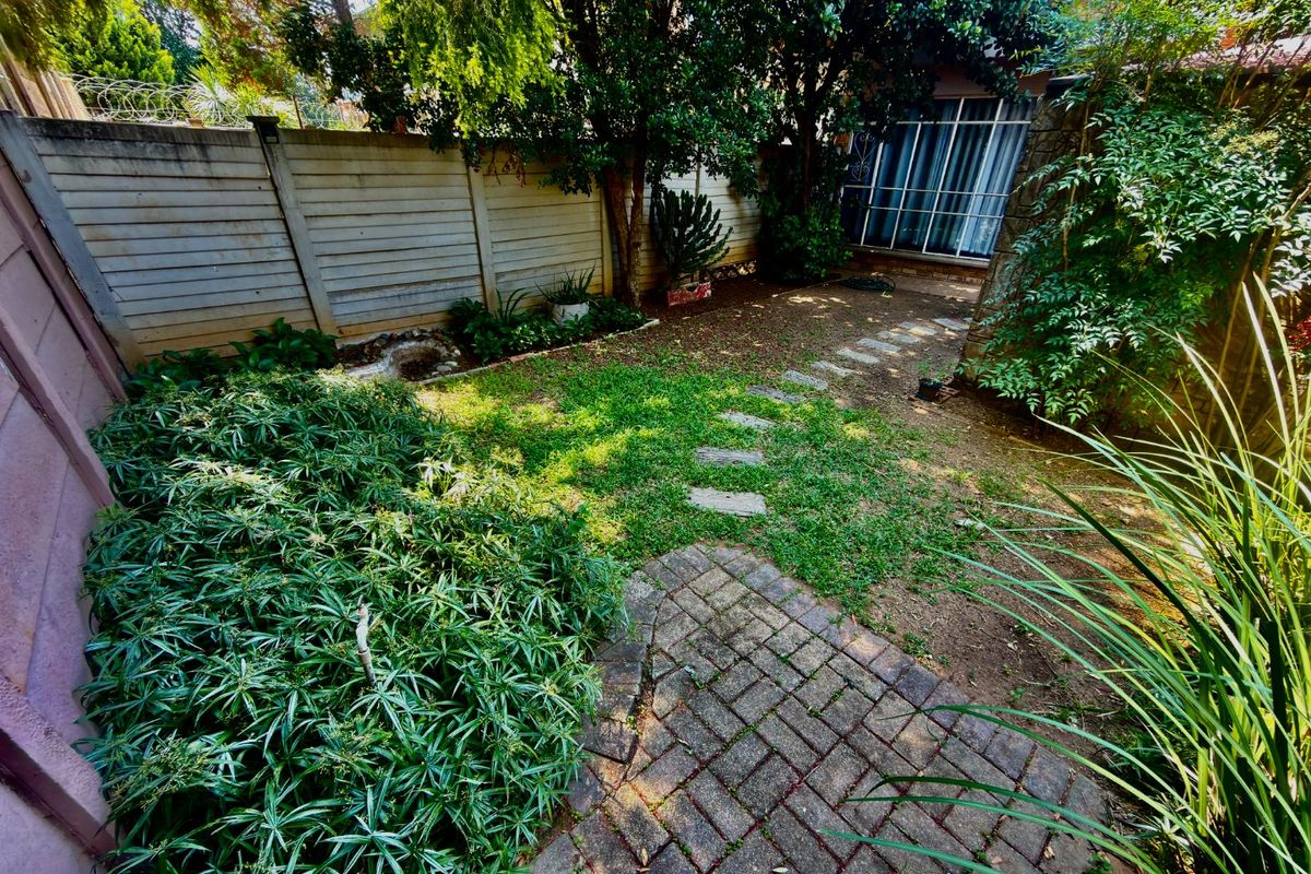 A private rear garden featuring a paved patio, stepping stone path, and established perimeter walling with mature trees and shrubs.
