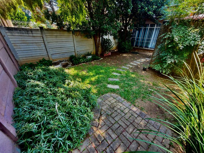 A private rear garden featuring a paved patio, stepping stone path, and established perimeter walling with mature trees and shrubs.