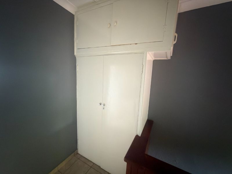 A bedroom space featuring a built-in wardrobe with additional overhead storage cupboards, finished with tiled flooring and dark grey wall paint.