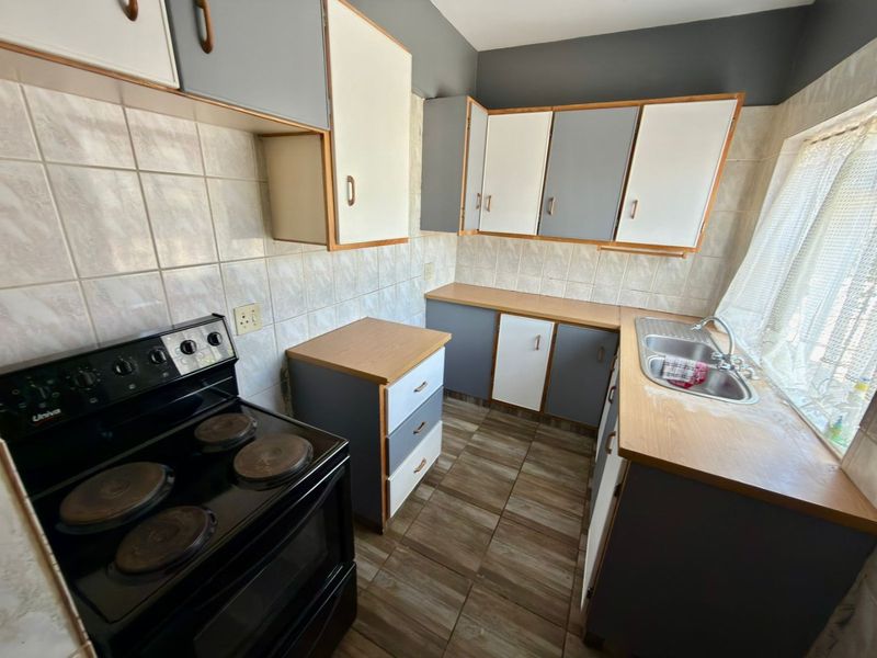 A functional kitchen featuring two-tone cabinetry, laminate countertops, a double stainless steel sink, and a freestanding electric stove with tiled backsplash and flooring.