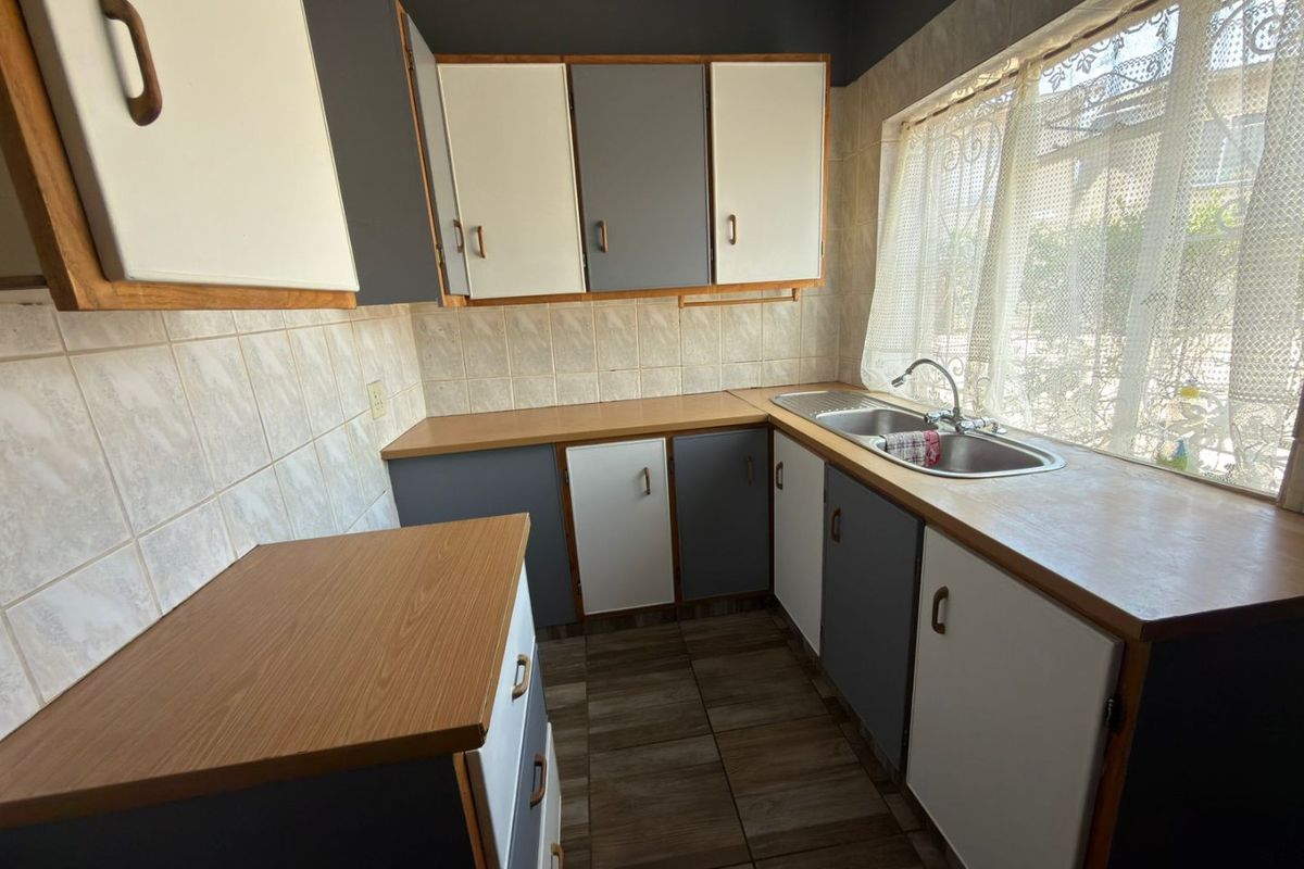 A functional kitchen featuring laminate countertops, a stainless steel double sink, tiled splashbacks, and ample built-in cabinetry with a neutral two-tone finish.