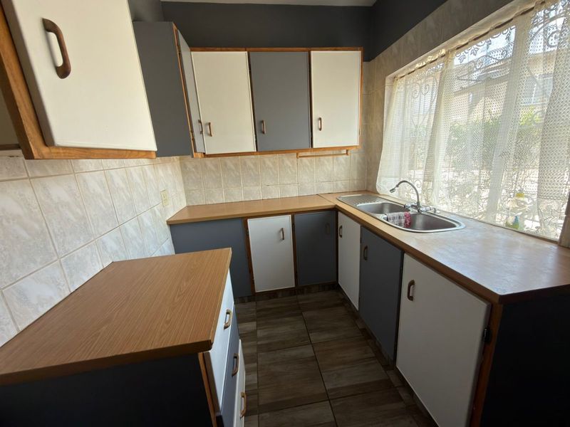 A functional kitchen featuring laminate countertops, a stainless steel double sink, tiled splashbacks, and ample built-in cabinetry with a neutral two-tone finish.