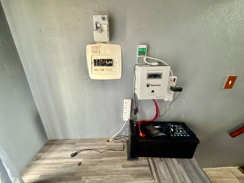Utility area featuring a wall-mounted electrical distribution board, prepaid meter, and a solar inverter system with backup battery on a laminate counter.