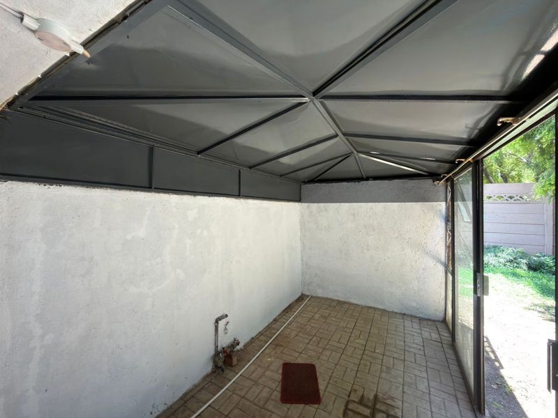 A covered patio area featuring paved flooring, a metal roof structure, and direct access to the garden through a sliding glass door.