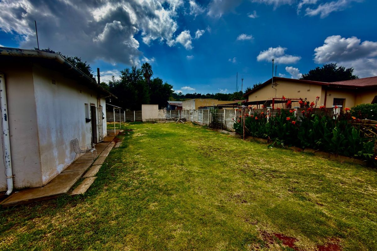 A rear garden area featuring a lawn, concrete pathway, and precast concrete boundary walls with visible exterior wall weathering.