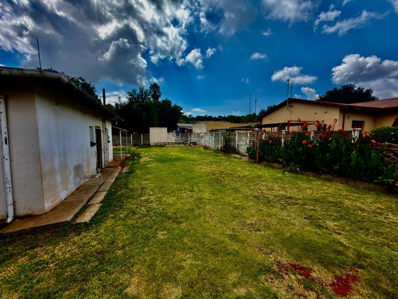 A rear garden area featuring a lawn, concrete pathway, and precast concrete boundary walls with visible exterior wall weathering.