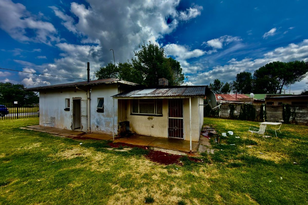 Rear view of a detached house featuring a covered patio area, corrugated metal roofing, and exterior walls showing significant signs of wear and weathering.