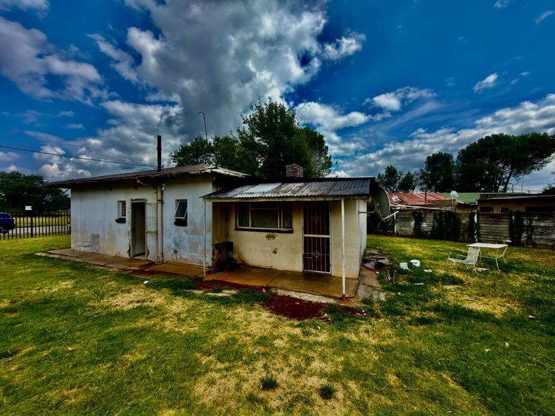 Rear view of a detached house featuring a covered patio area, corrugated metal roofing, and exterior walls showing significant signs of wear and weathering.