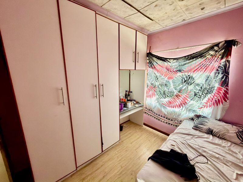 A bedroom featuring built-in cupboards with an integrated vanity area and laminate flooring. The room requires cosmetic updates to the ceiling and finishes.