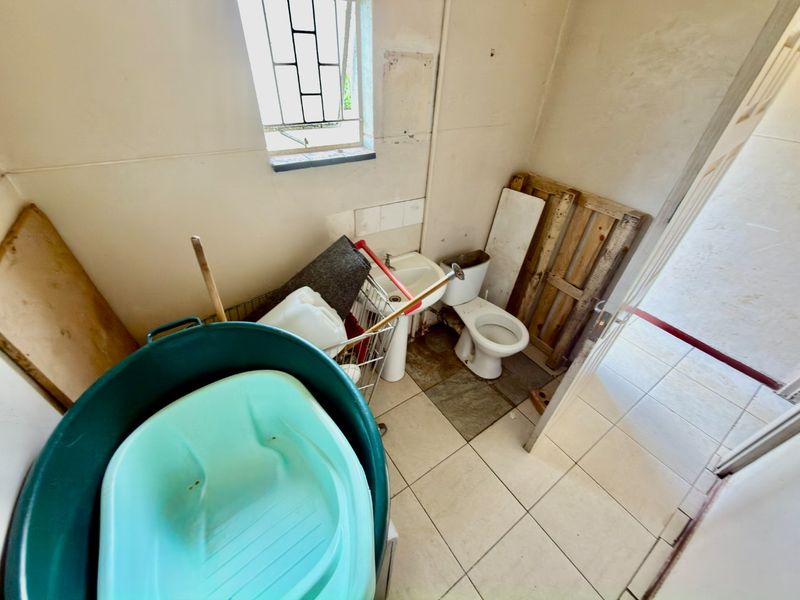 A small bathroom featuring a toilet and pedestal basin, requiring renovation and cosmetic updates to improve the overall condition and functionality of the space.