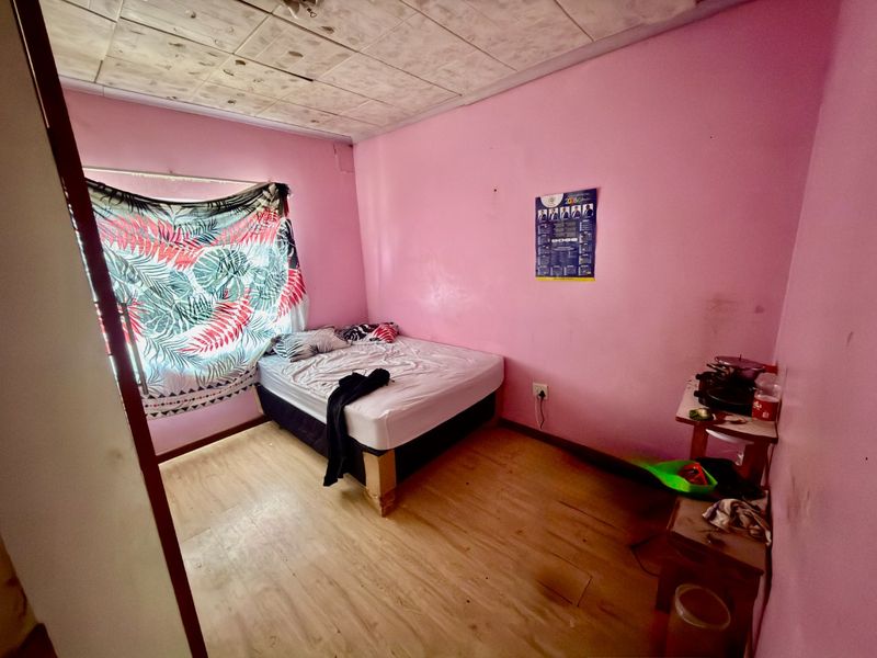 A bedroom featuring laminate flooring and a tiled ceiling, currently requiring maintenance and cosmetic updates to improve the overall condition of the space.