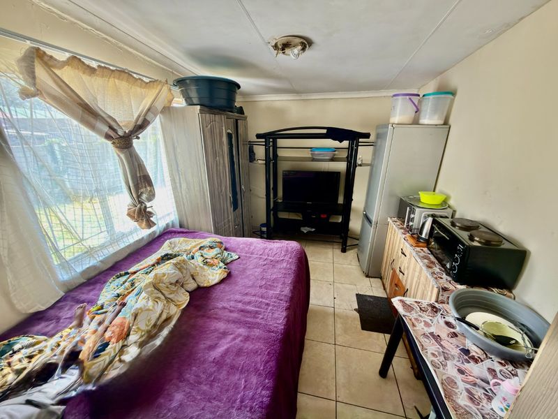 Compact open-plan living and sleeping area featuring ceramic floor tiles and a window, requiring cosmetic updates to improve the overall condition.