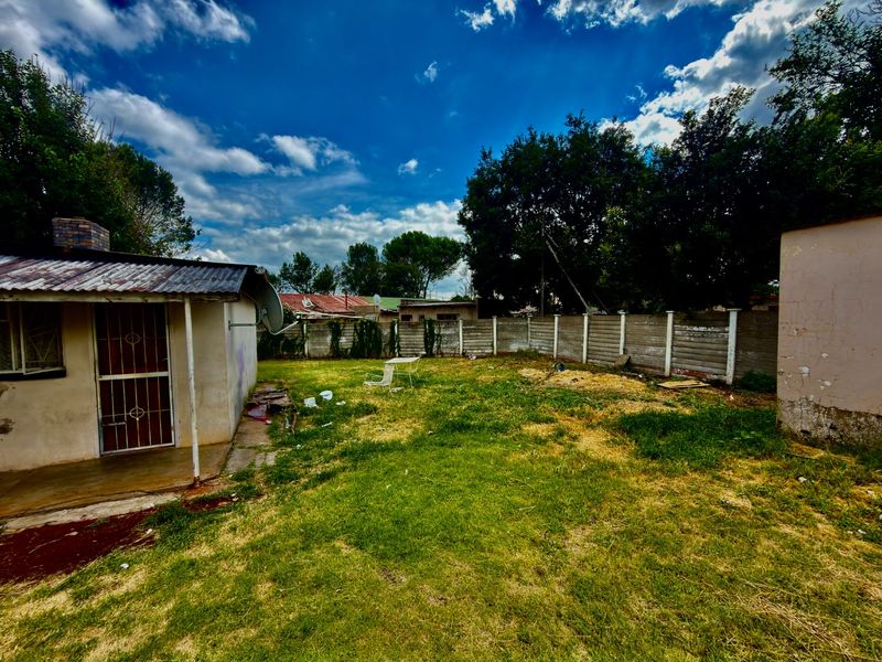 Rear garden area featuring a precast concrete boundary wall, corrugated metal roof structure, and security gate access.