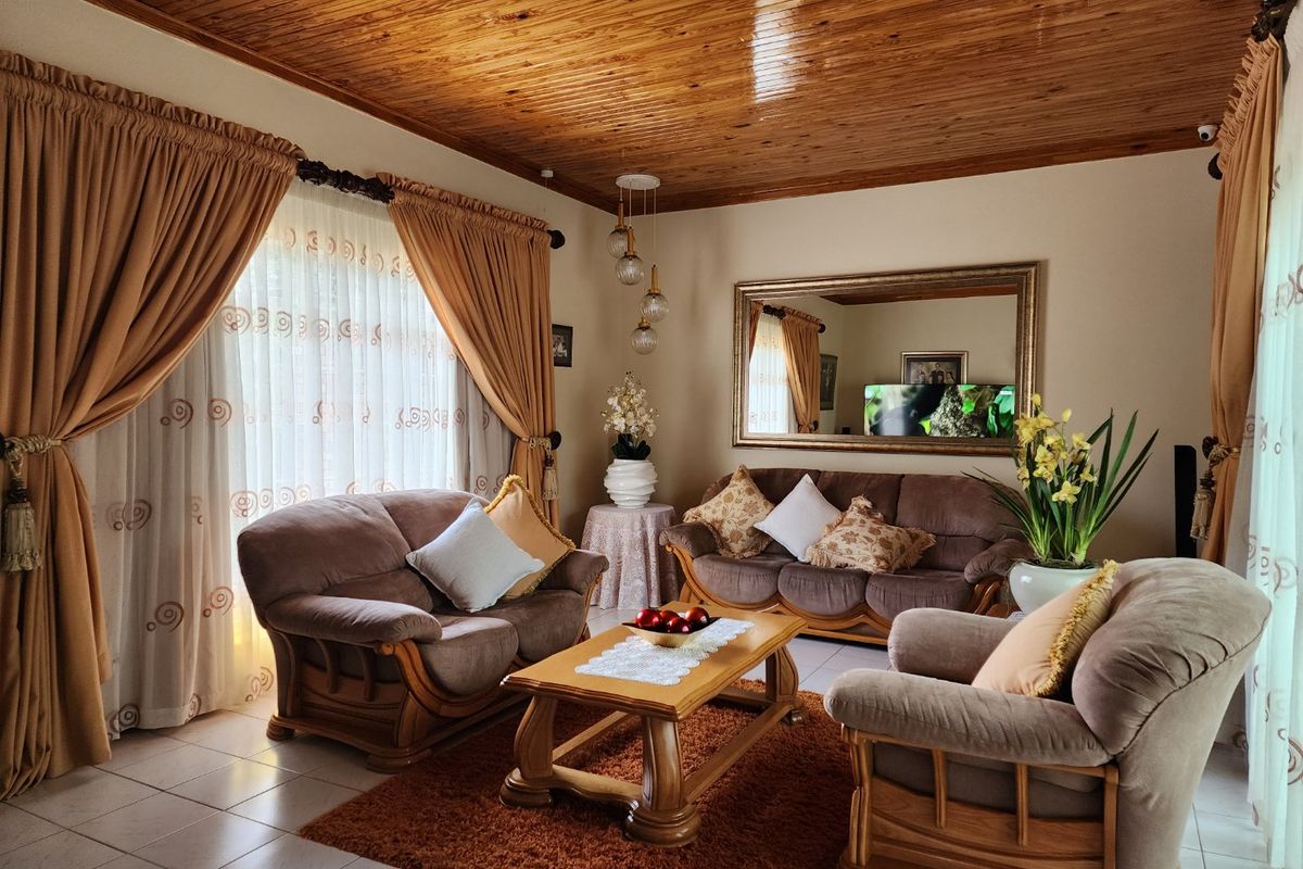 A cozy living room featuring a polished timber-clad ceiling, tiled flooring, and large windows with draped curtains, creating a warm and inviting atmosphere.