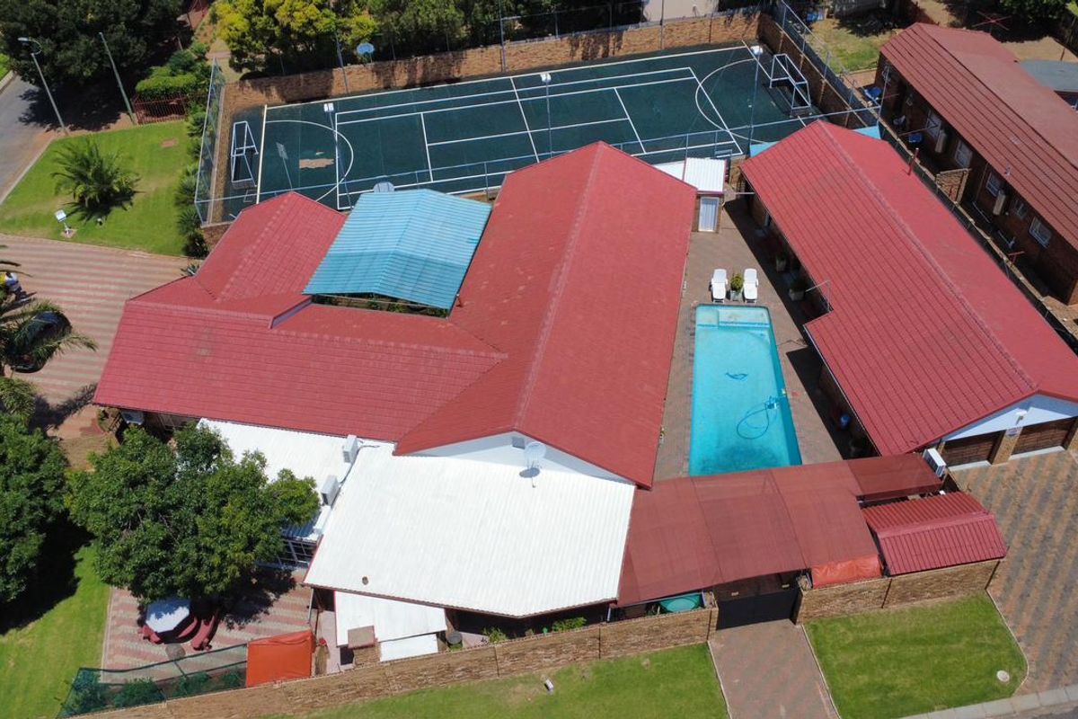 Aerial view of a residential property featuring a swimming pool, large red-roofed structure, and an adjacent private sports court.