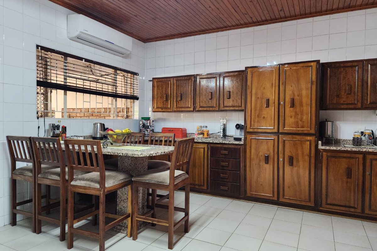 A functional kitchen featuring traditional timber cabinetry, granite countertops, tiled flooring, and a timber-paneled ceiling, equipped with a wall-mounted air conditioning unit.