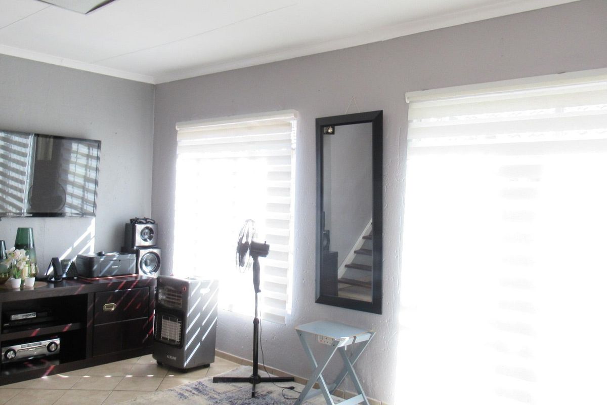 A bright living room featuring tiled flooring, dual windows with fitted roller blinds, and a neutral wall finish.
