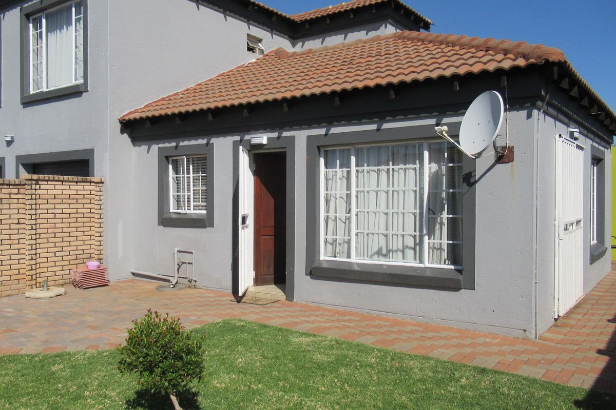 Rear view of the property featuring a paved patio area, small garden, and access to the main dwelling with tiled roof.