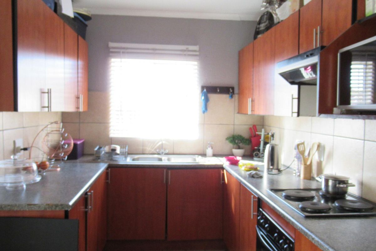 A functional galley-style kitchen featuring wood-finish cabinetry, tiled splashbacks, a built-in electric hob, and an integrated oven.