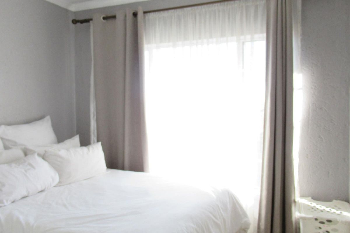 A bedroom featuring neutral wall tones and a window with curtain treatments, providing natural light.