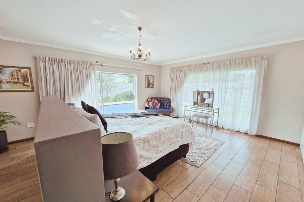 Spacious bedroom featuring wood-look tiled flooring, a central chandelier, and large sliding glass doors providing direct access to the pool area.