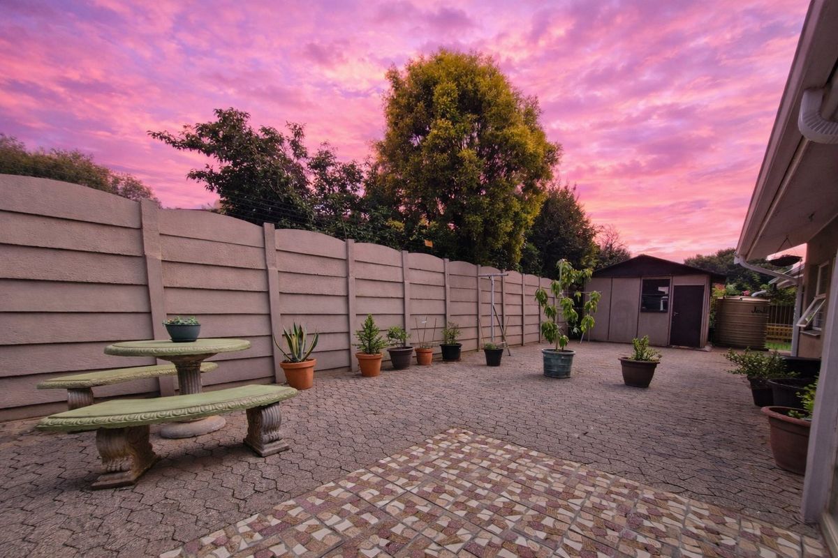 A paved rear courtyard featuring a precast concrete boundary wall, a storage shed, and a water tank under a vibrant sunset sky.