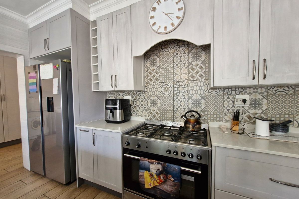 Modern kitchen featuring light grey cabinetry, patterned tile backsplash, stone countertops, and a stainless steel gas stove with oven.